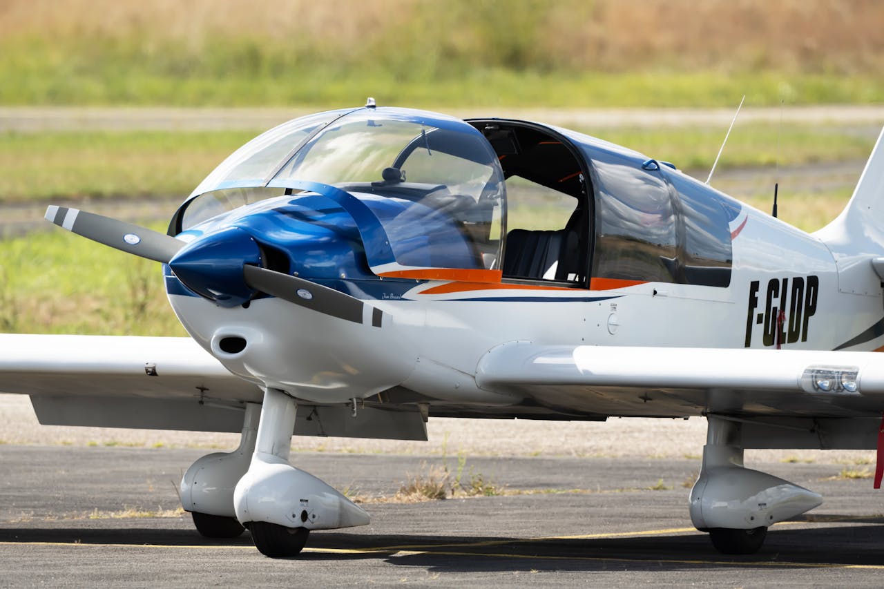 portfolio-05 White and blue light aircraft parked on tarmac with open canopy, ready for flight.